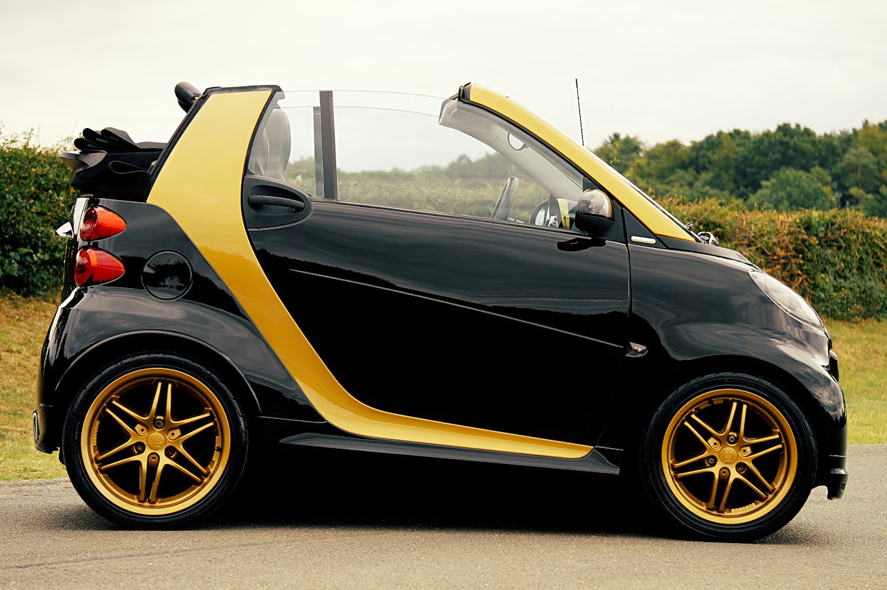 Sleek black and gold convertible car parked outdoors with stylish design and shiny rims.
