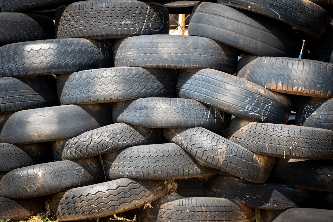 Pile of black rubber tires stacked outdoors in daylight.