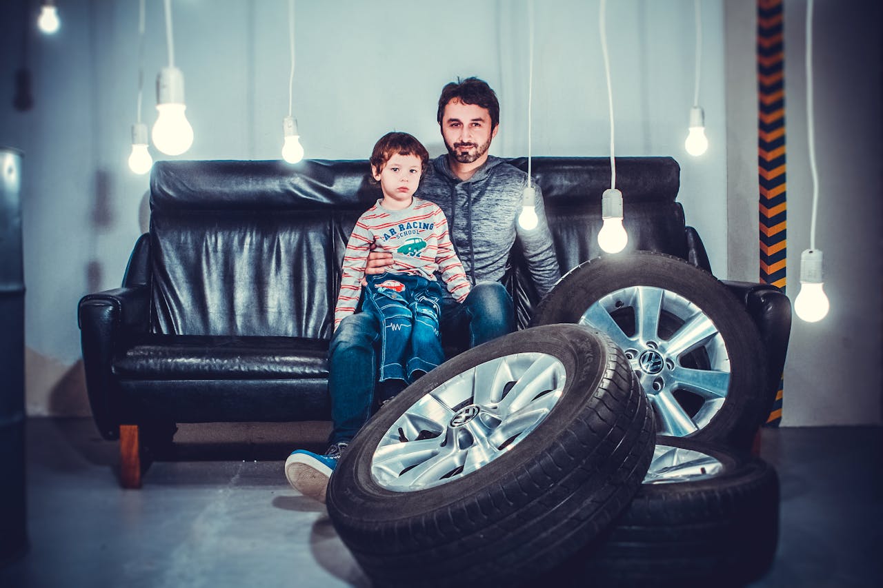 Father and son sitting on a sofa surrounded by hanging lights and car tires in a modern studio.