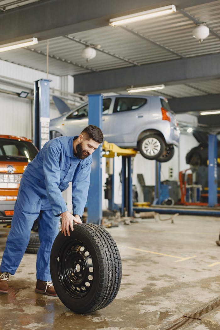 who-we-are Mechanic handling a tire in a busy automotive repair workshop.